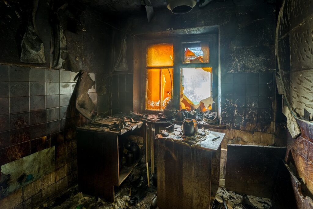 Fire damaged kitchen interior with charred walls and broken window in NYC apartment