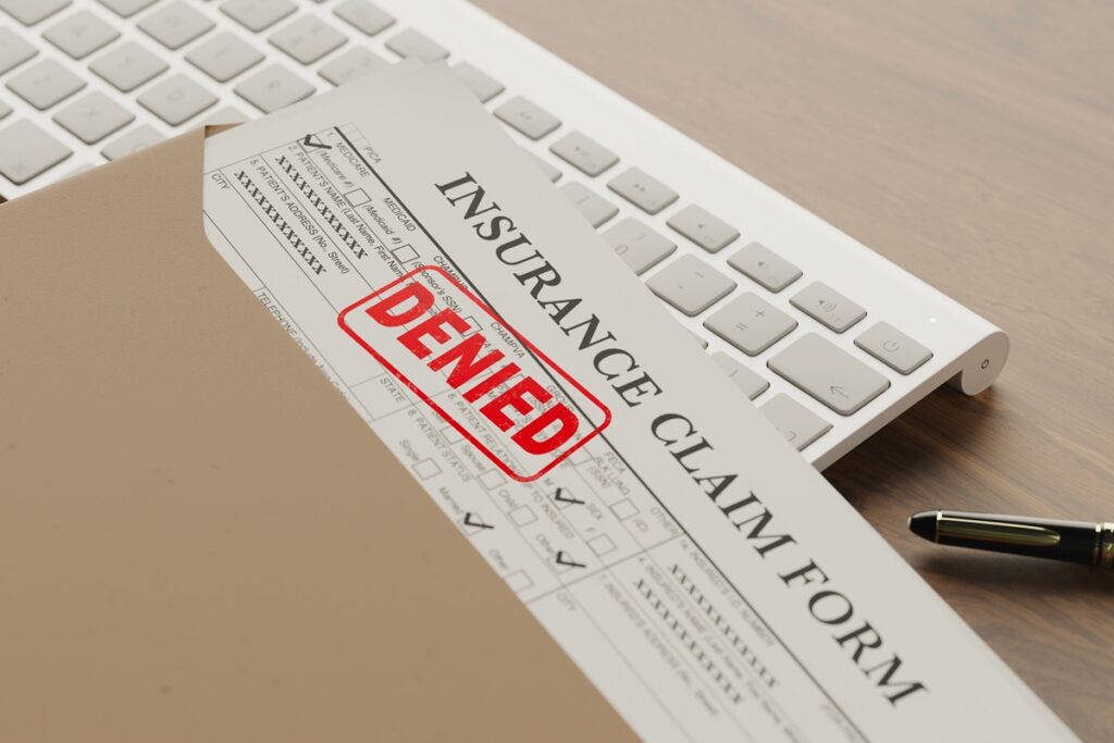 Insurance claim form stamped DENIED in red ink on a desk